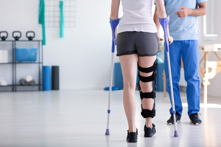 Patient with stiffener on the leg walking with crutches during rehabilitation